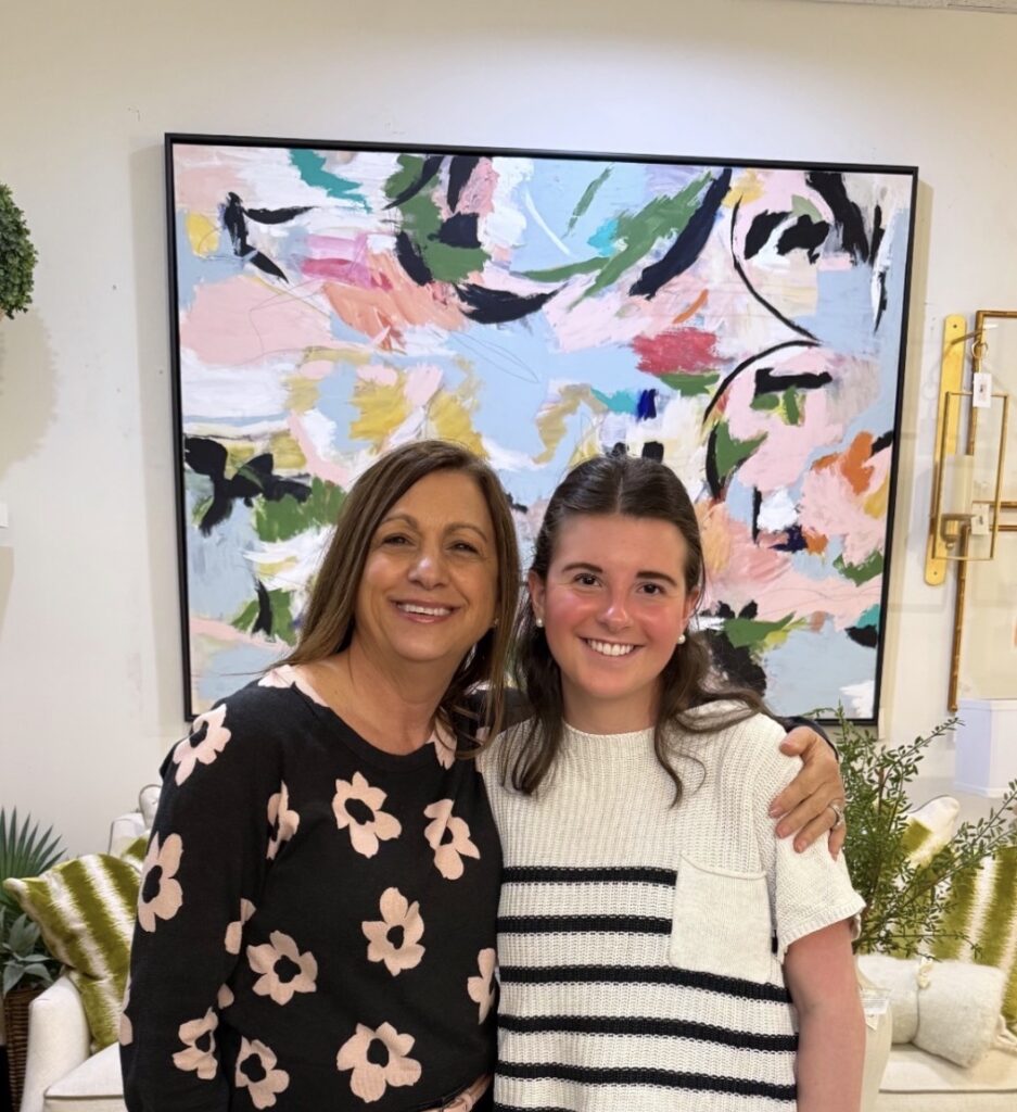 Two smiling students in classroom with colorful abstract art behind them.