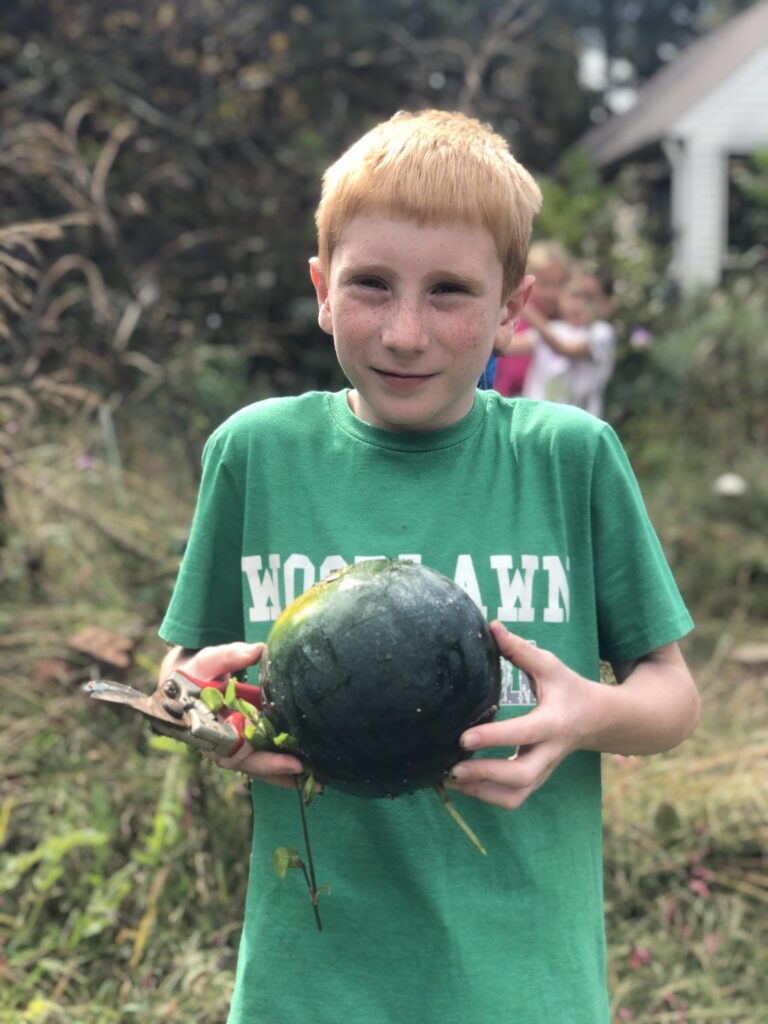 Lower School student holding a watermelon he harvested from the Woodlawn School garden.